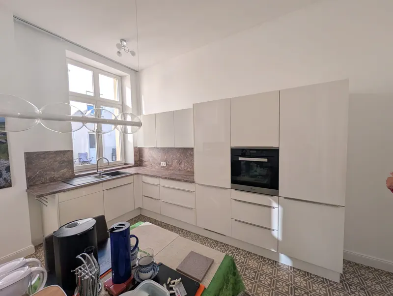 Weiße Küche mit Hochschrank, Einbaubackofen und Steinarbeitsplatte